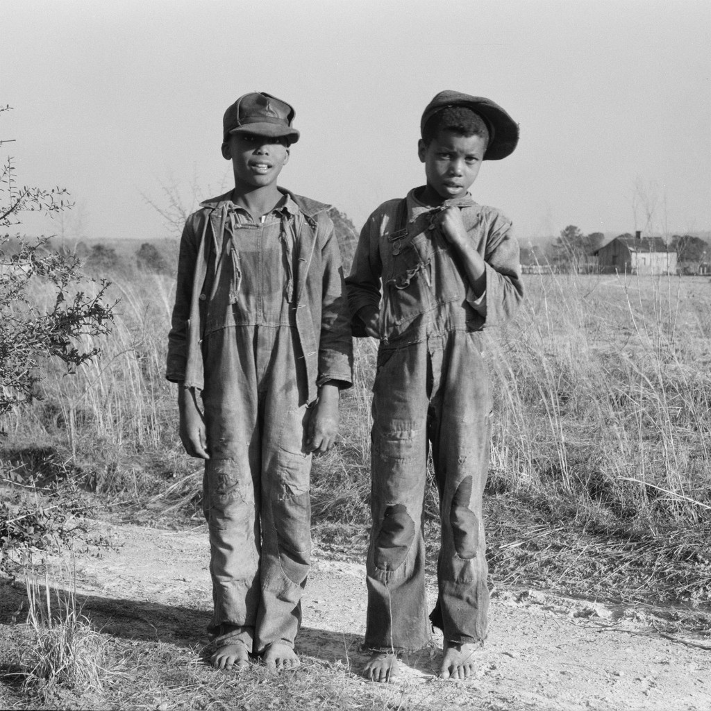Two young Black boys wearing overalls in a field