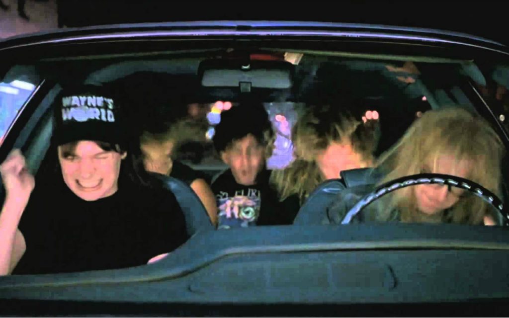 A still from Wayne's World shows Mike Myers and Dana Carvey as Wayne and Garth headbanging in the car to Queen's Bohemian Rhapsody
