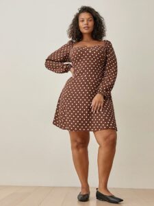 A model wearing reformation's brown with white polka dots, long sleeves and a sweetheart neckline dress with black flats
