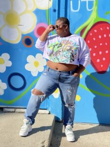 London Blackwood wears a secondhand crop top in front of a brightly-painted wall.
