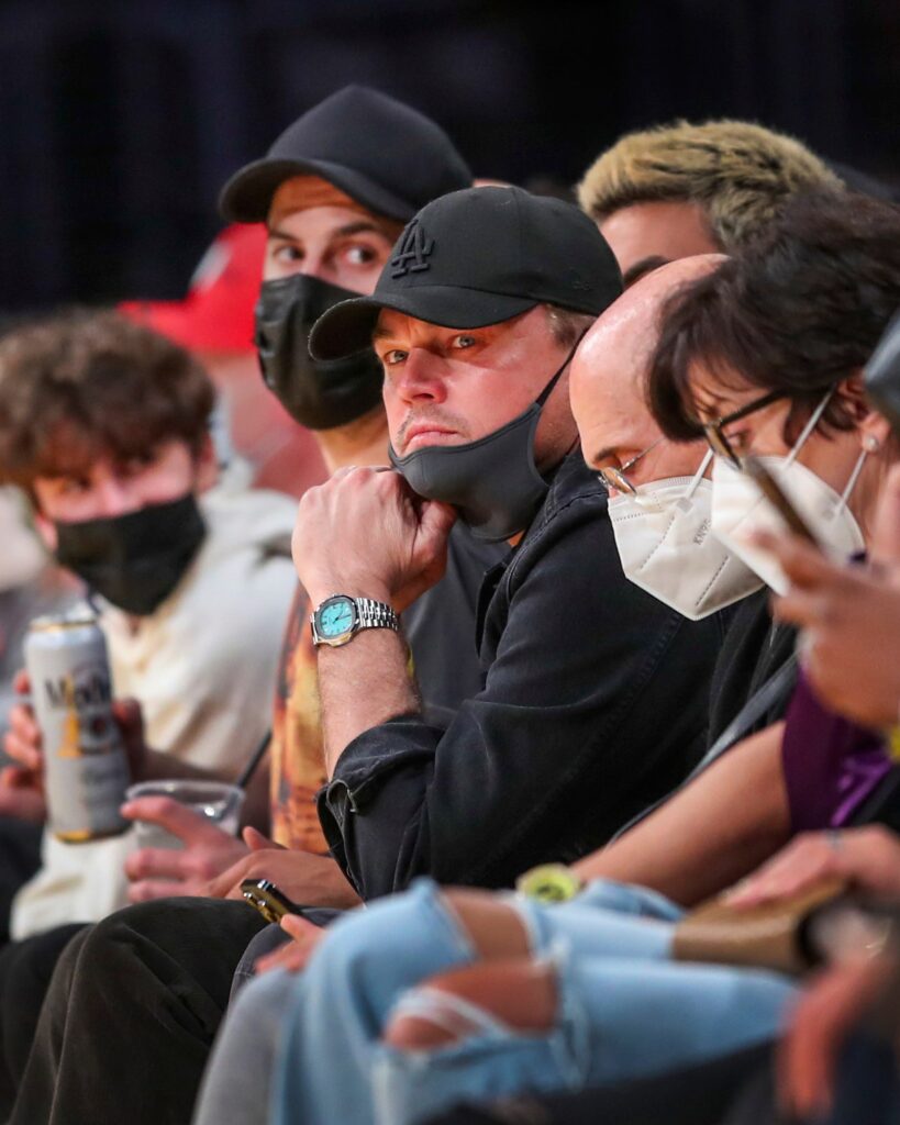 Leonardo DiCaprio center in black hat with mask partly down sits next to film producer Jeffrey Katzenberg right of him...