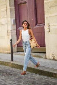 PARIS, FRANCE - JULY 20: Alexandra Pereira wears brown sunglasses from Tod's, a white ribbed tank top, a beige large wicker bag from Vuitton with printed monograms, pale blue denim ripped jeans pants, brown leather Hermes Oasis sandals / shoes, on July 20, 2021 in Paris, France. (Photo by Edward Berthelot/Getty Images)