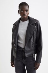 A model in a black faux leather biker jacket, grey t-shirt, black jeans and hoop earrings
