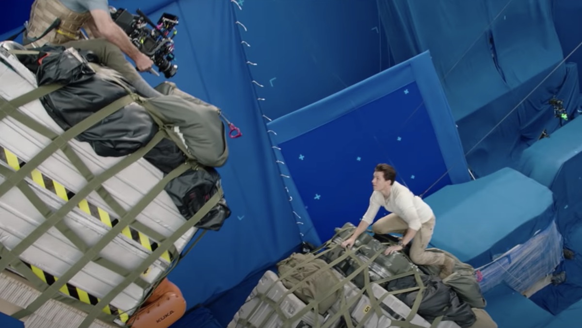 Tom Holland on a cargo box against a blue screen as a camera films in for Uncharted