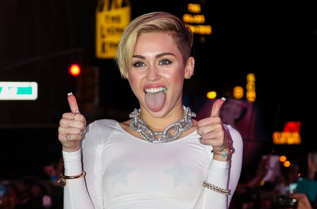 Miley Cyrus posing with her thumbs up and tongue out in 2013