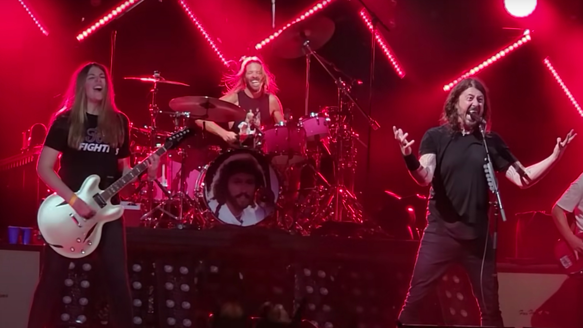 A young fan playing guitar on stage alongside Dave Grohl at a live show.