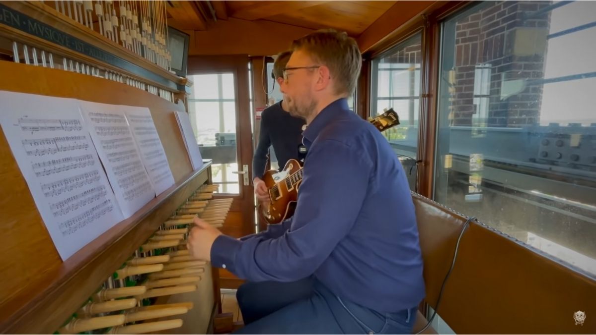 A man playing a piano in a church with a man playing guitar in the background