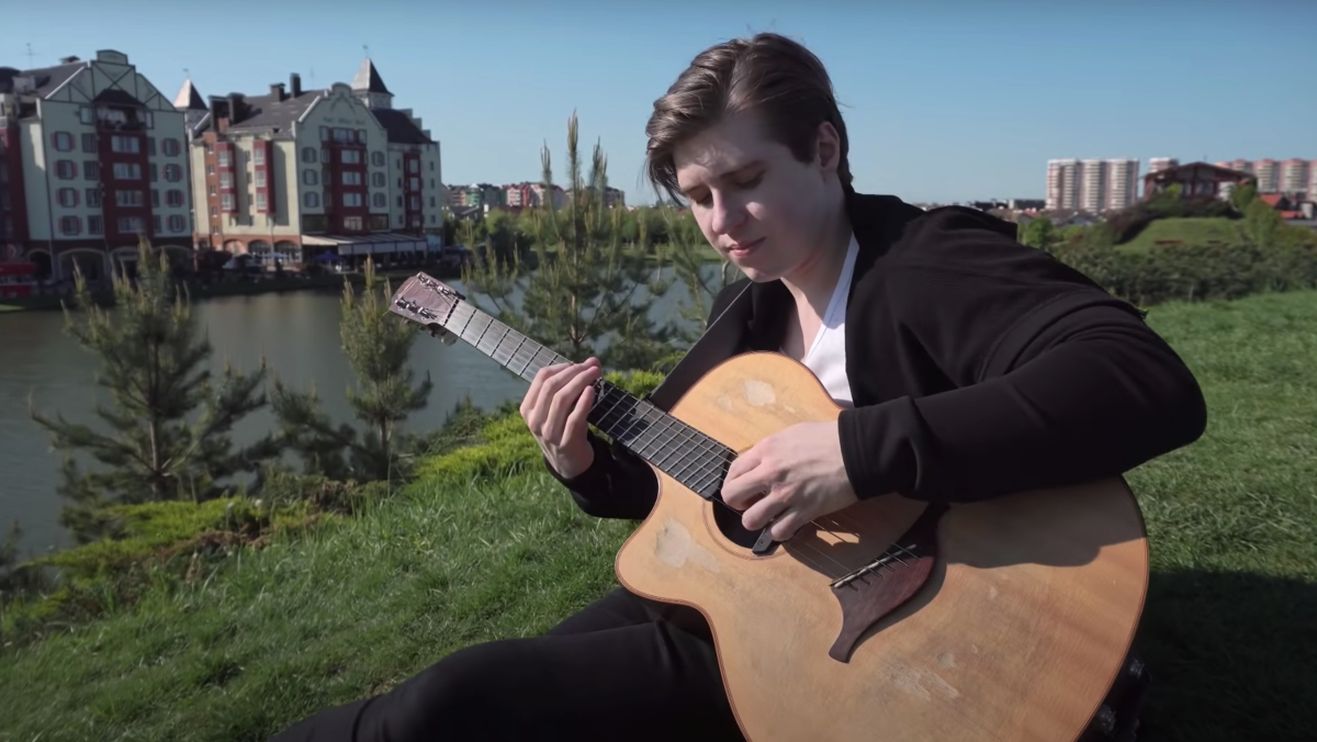 Guitarist Alexandr Misko plays his guitar in front of a river and homes.