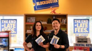 Randall Park and Melissa Fumero stand behind Blockbuster store counter holding DVDs in first look photo for Netflix series