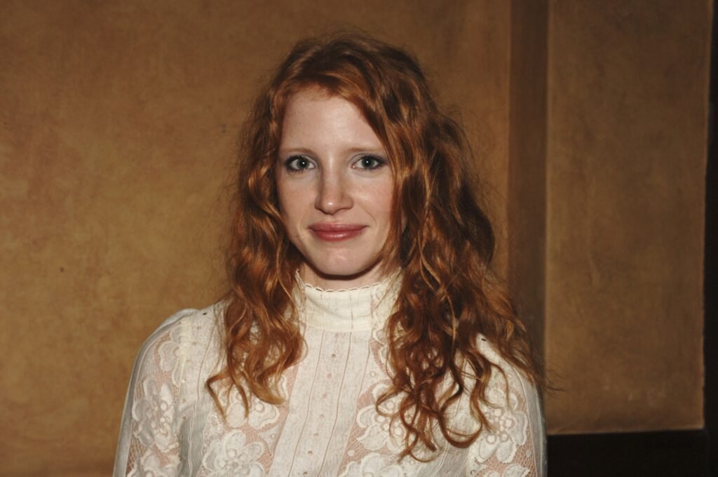 Jessica Chastain smiles. She is wearing a turtleneck lace top and her curly red hair is down.