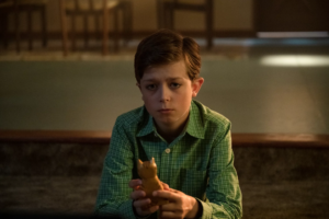 An image from Umbrella Academy Season Two shows Harlan a young non-verbal child sitting looking sadly towards the camera