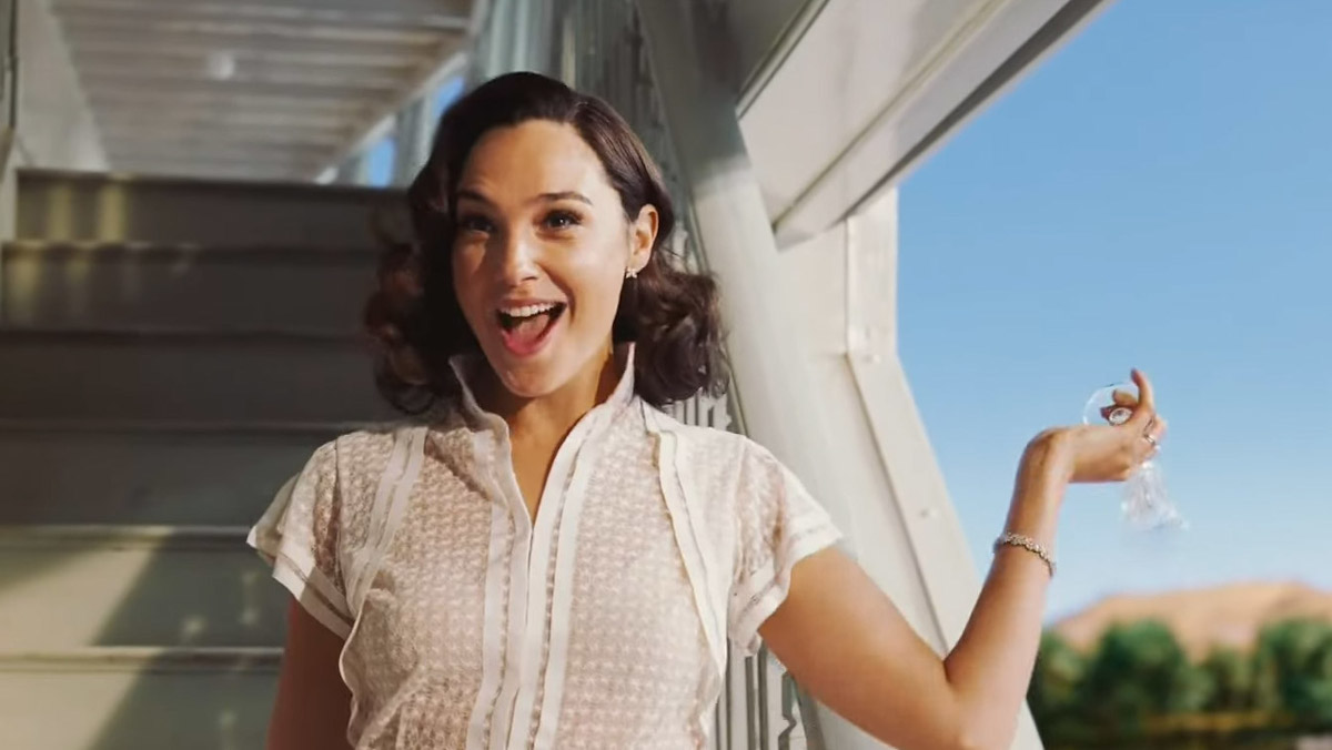 Gal Gadot in a screenshot from Death on the Nile, throwing champagne into the Nile and saying they could fill the Nile