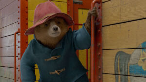 Paddington the bear holds onto a red rail