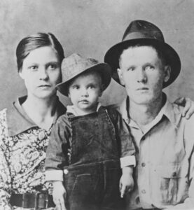 Black and white photo of a young toddler with his mother on his left and father on his right