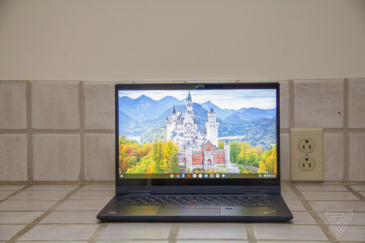 The Lenovo ThinkPad C13 Yoga Chromebook seen from the front on a tile counter. The screen displays a white castle surrounded by trees with mountains in the background.