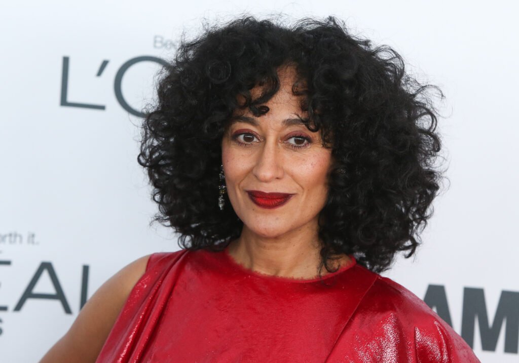 Tracee Ellis Ross smiling in red gown against white backdrop