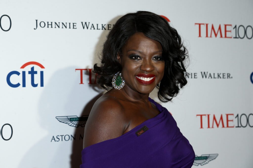 Viola Davis smiling in purple gown against white backdrop