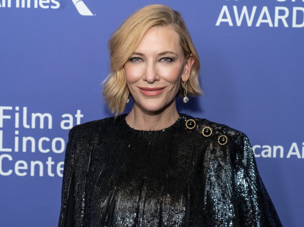 Cate Blanchett smiling in black sequined dress against blue backdrop