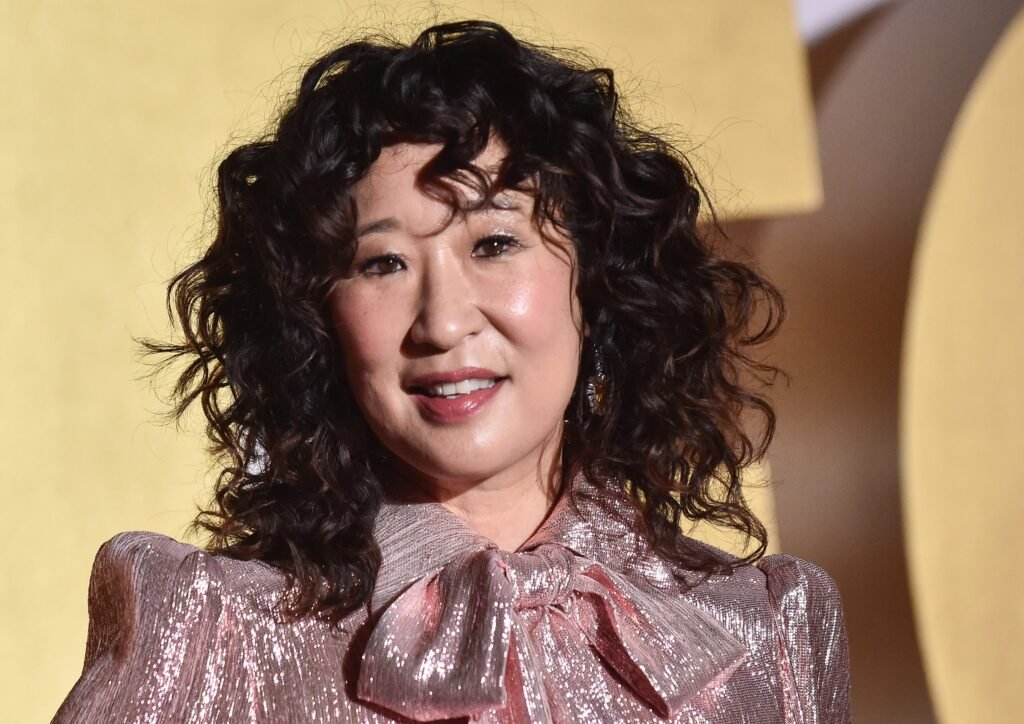 Sandra Oh smiling in rose-gold top against yellow backdrop