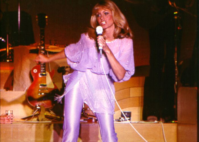Olivia Newton-John performing onstage in shimmery purple leather outfit