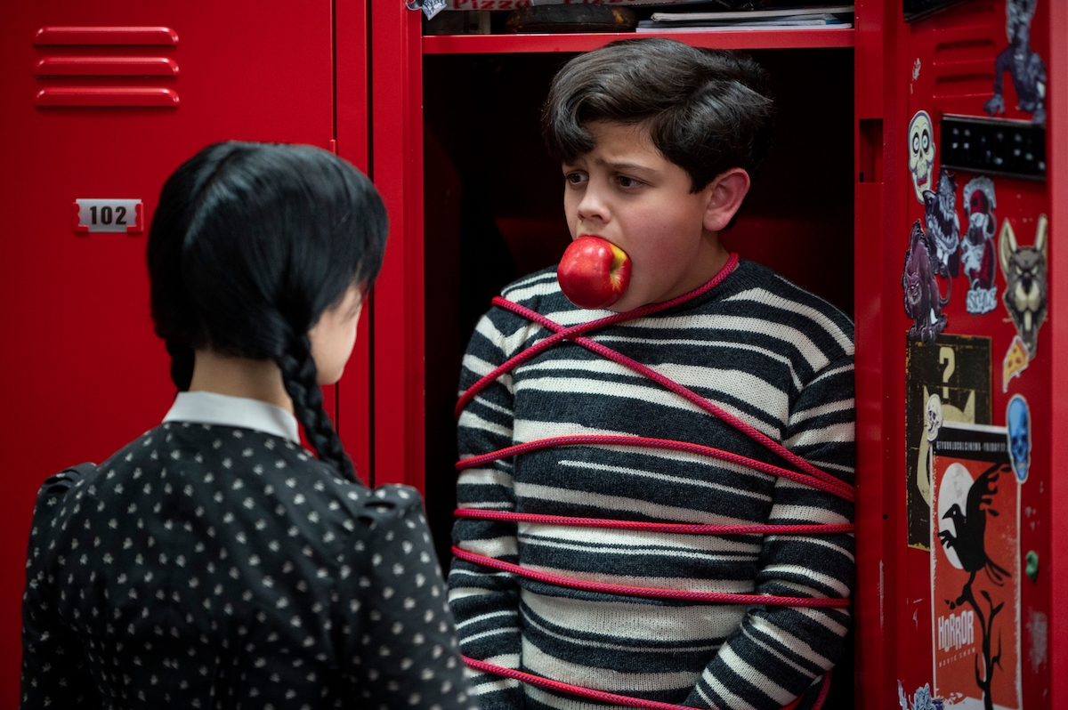 Pugsley is tied up in his locker with an apple in his mouth as his sister Wednesday looks at him