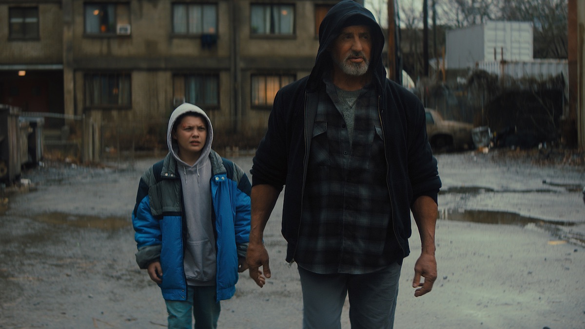A hooded Joe (Sylvester Stallone) walks in front of his young neighbor Sam in Samaritan