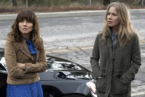 Two women standing outside a car by the side of the road.