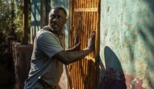 Idris Elba stands against a locked, rusty exterior door, nervously looking over his shoulder in Beast