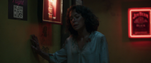 A bedraggled Jen Walters (She-Hulk, played by Tatiana Maslany) leans on a wall in a bar in She-Hulk. There’s a sticker on the wall with a visible QR code on it.