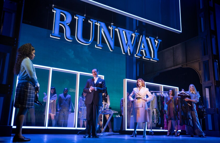 People onstage in a stylized office under the word "Runway"