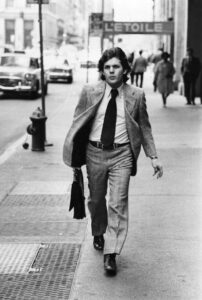Black and white photo of a man in a suit walking in a city