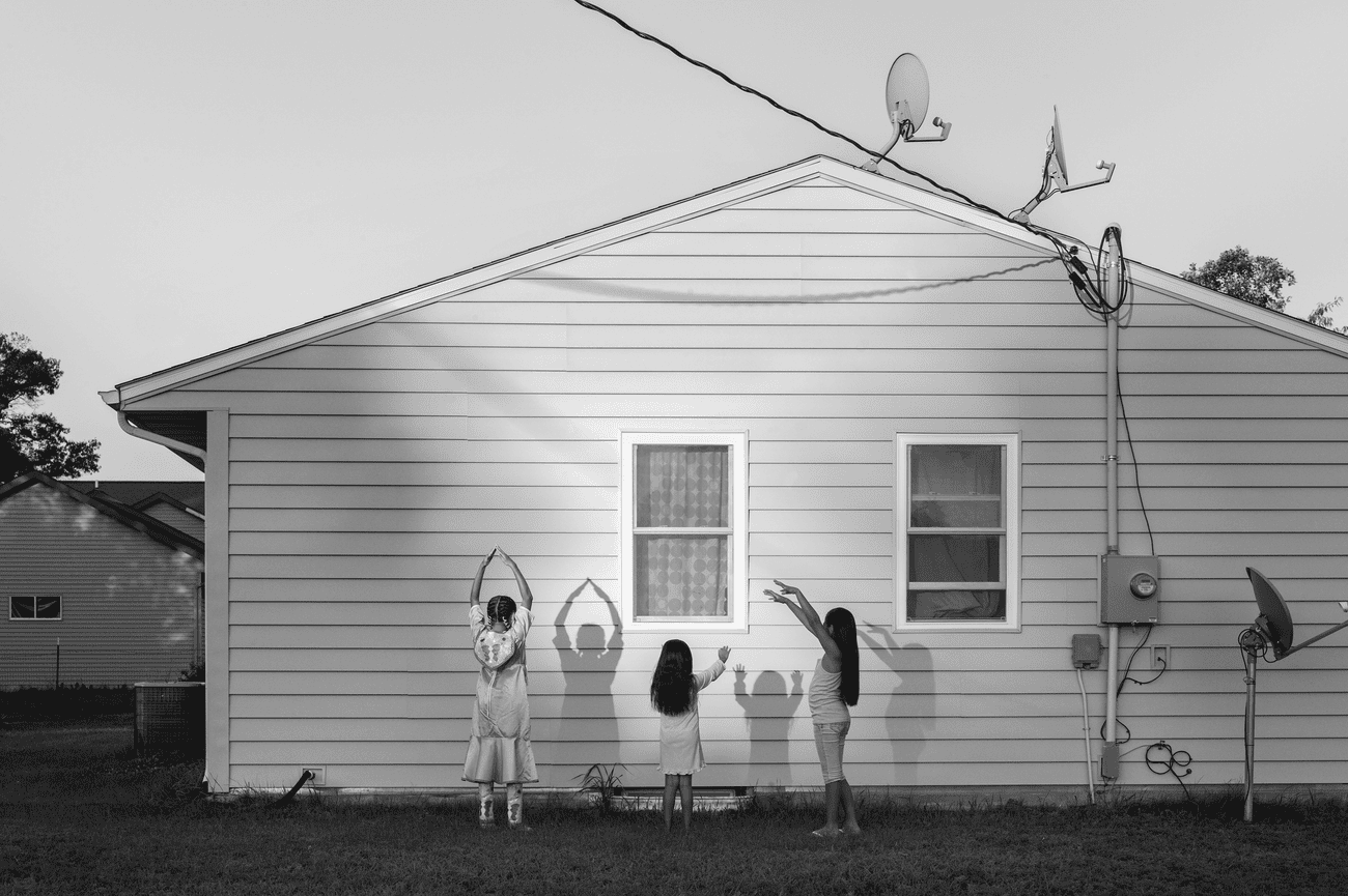 Three young girls making shadows on the side of a wooden house