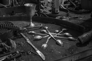 Spoons and a metal goblet amid tools on a workbench