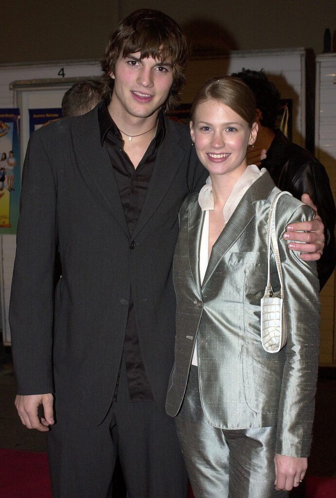 Ashton Kutcher (L) in all-black suit with his arm around January Jones, who is wearing a silver blazer