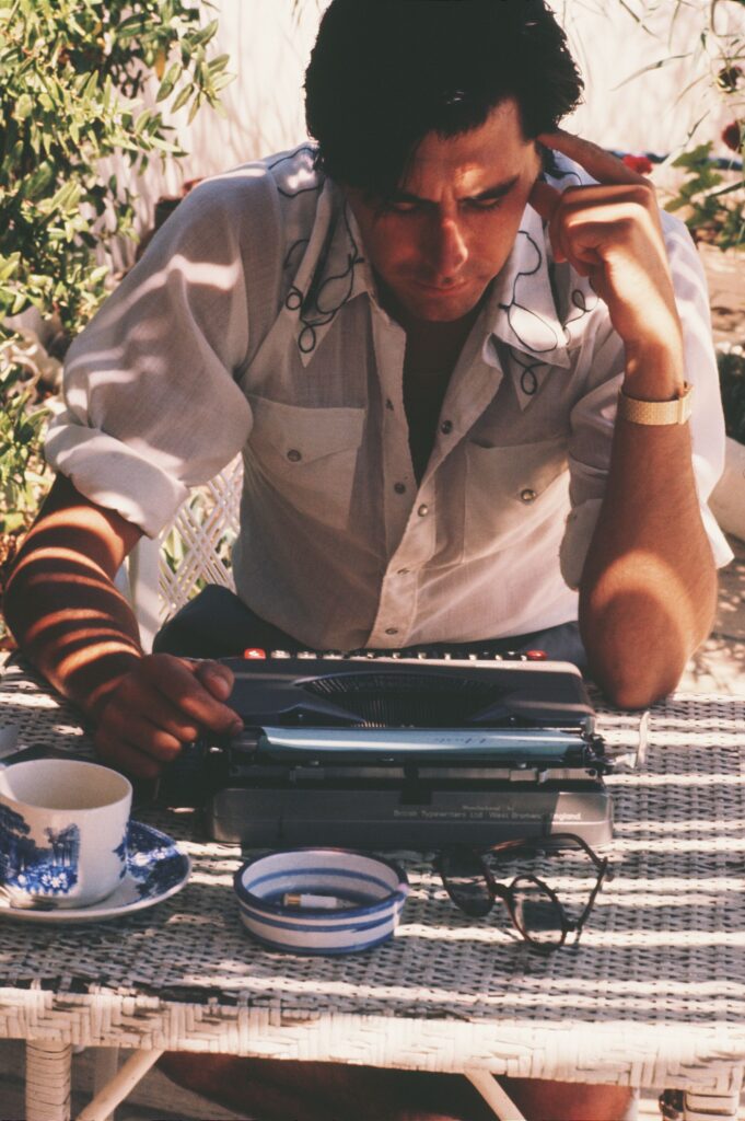 A man in the 1970s stares down at a typewriter