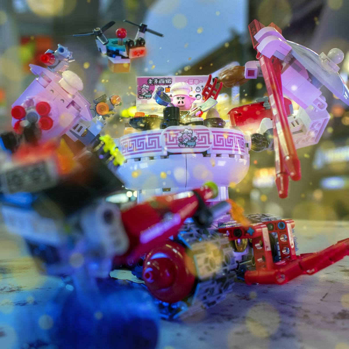 A lego pig chef works in a giant wheeled contraption built to look like a noodle bowl complete with arms wielding chopsticks and drone sidekick