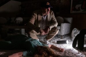 Fletch (Jon Hamm) crouches over an unexpected woman’s corpse in his apartment in Confess, Fletch