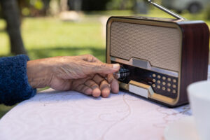 An older person's hand adjusting the volume of music on a radio.