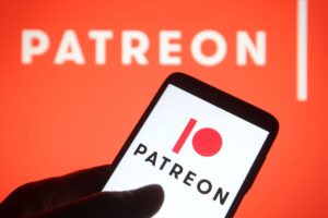 In this photo illustration, a Patreon logo is seen on a smartphone in front of a larger Patreon logo on an orange background.