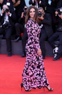 Penelope Cruz on red carpet in longsleeved black dress with pink leaves all over it