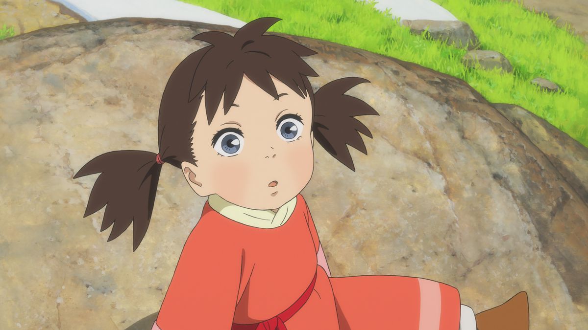 A little girl with big blue eyes and brunette pigtails wearing a salmon-colored robe looks up from where she’s sitting on a rock