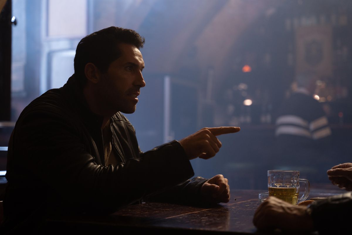 Scott Adkins points his finger while seated at a bar table in Accident Man: Hitman’s Holiday