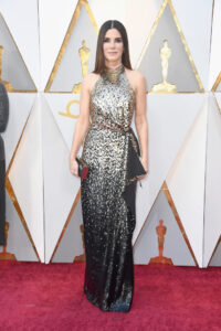 Sandra Bullock standing on red carpet in gold and black sequined gown