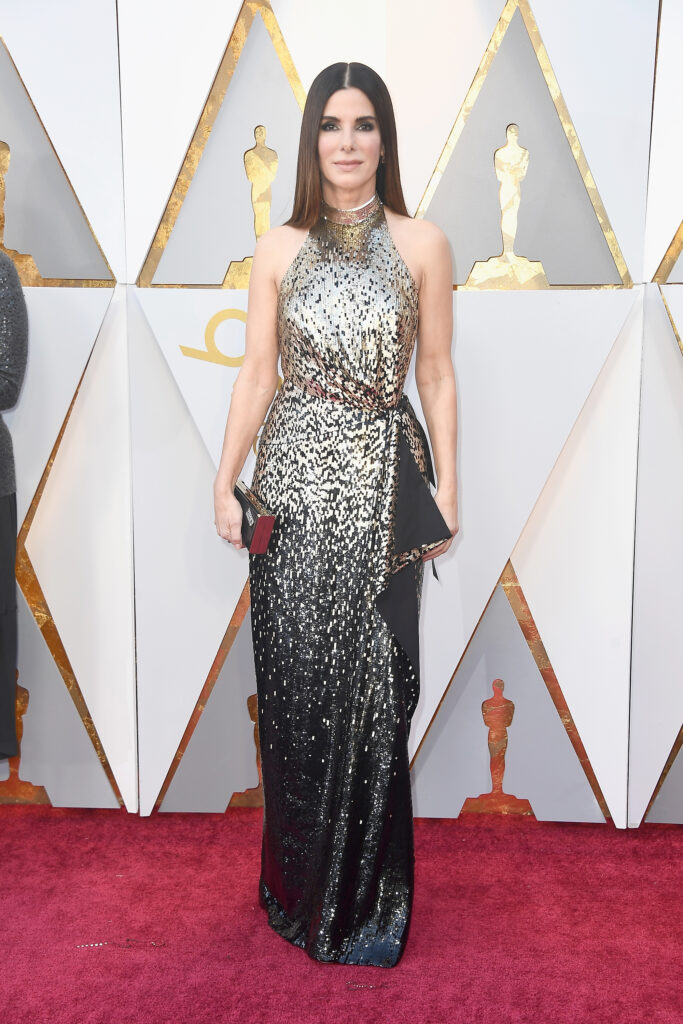 Sandra Bullock standing on red carpet in gold and black sequined gown