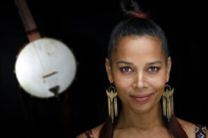 A portrait of Rhiannon Giddens with a banjo hanging in the background.