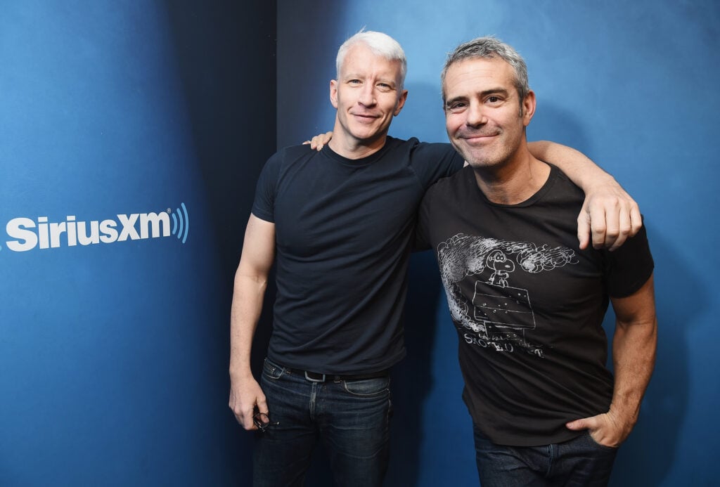 Andy Cohen (R) in black tee shirt and his arm around Anderson Cooper, who is wearing a dark tee shirt