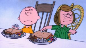 charlie brown and peppermint patty sit at a table in front of Thanksgiving meal