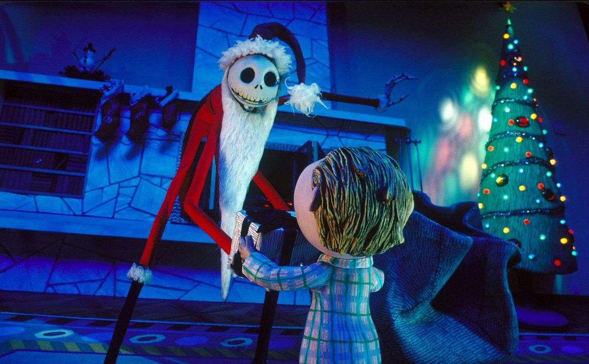 A tall skeleton-like figure in a Santa Claus outfit knells before a young boy in a living room with a Christmas tree in the background.