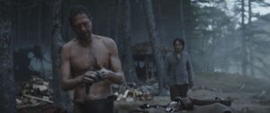 Seen stands shirtless, tinkering with a device in the Rebel camp while Cassian Andor walks towards him from behind