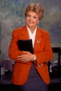 A woman in a red blazer smiling and holding a black book